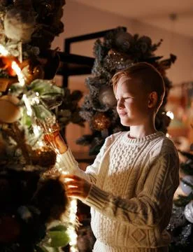 Cute small boy kid decorating Christmas tree at home in evening, vertical image 库存照片