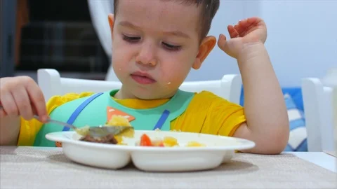 Cute Small Child is Sitting at a Table in a Bib and Eat His Own Puree, the Baby Stock Footage 104560569
