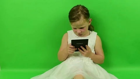 Cute small girl reads e-book on chroma key background. Little girl dressed in a Video stock 81749412