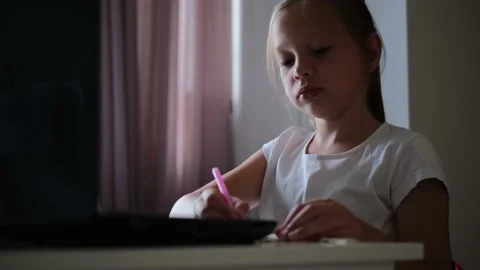 Cute smart elementary school child girl doing math homework sits at home behind Video stock 134714418