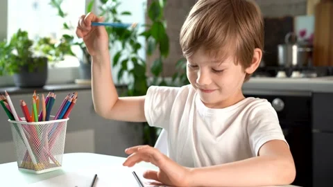 Cute smiling boy draws with colored pencils, at home at the table, happy baby Stock Footage 155525393
