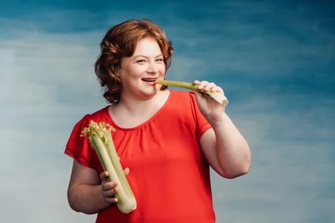 Cute smiling chubby red-haired girl bites celery and smiles Stock Photos
