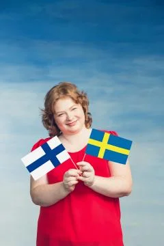 Cute smiling chubby red-haired woman holdingflags of Sweden and Finland on a  Stock Photos