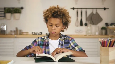 Cute smiling mixed race kid is sitting at table in kitchen and looking straight Stock Footage 114019095