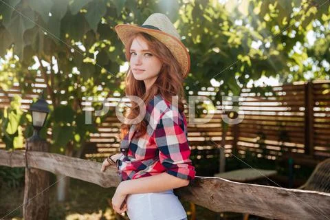 Cute smiling redhead cowgirl in hat leaning on ranch fence Stock Photos