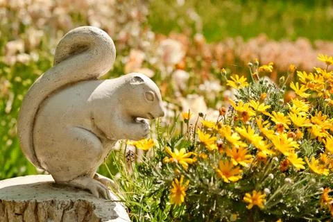 A cute stone chipmunk statue made of stone in a yard setting with flowers Stock Photos