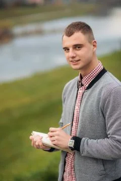 A cute student writes down his thoughts in his notebook using a pencil. The guy Stock Photos