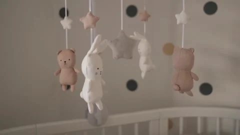 Cute stuffed baby animals rotating above white wooden crib in nursery Stock Footage 263098495
