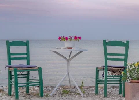 Cute table and chairs for two with flowers, sea, beach and sunset Stock Photos