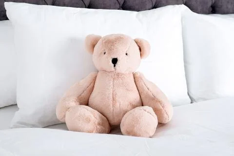 Cute teddy bear sitting on bed indoors Stock Photos