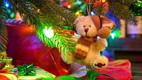 A cute teddy bear wearing a red hat and scarf is hanging on a Christmas tree  Stock Photos