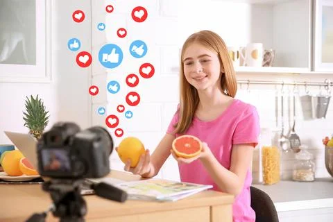 Cute teenage blogger with fruits recording video at table Stock Photos