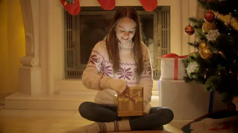 Cute teenage girl sitting at fireplace and opening Christmas gift box Stock Footage