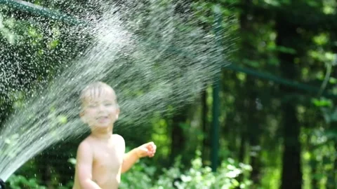 Cute toddler blond boy playing with garden sprinkler on summer hot day. Stock Footage 134194000