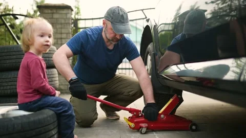 Cute toddler boy helping his father to change car wheels at their backyard. Stockbeeldmateriaal 198212840