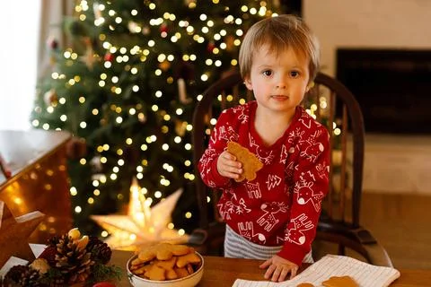 Cute Toddler Boy Standing by Table Holding Homemade Gingerbread Cookie. Chr.. 스톡 사진