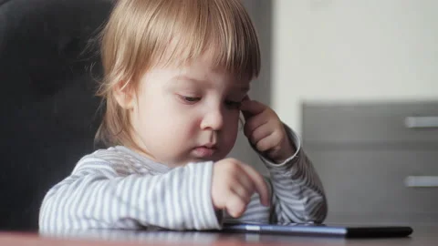 Cute toddler boy using a digital device while sitting at a desk. Children's Stock Footage 151590740
