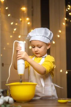 Cute toddler boy using hand blender to dough to cake . Preparing healthy meal in Foto stock