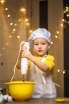 Cute toddler boy using hand blender to dough to cake . Preparing healthy meal in Stock Photos