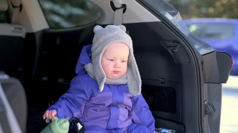 Cute toddler dressed in warm winter clothes, sitting in the trunk of a car and Stock Footage 280370168