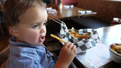 A cute toddler eating delicious french fries at fast food restaurant Stock Footage