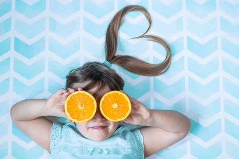 Cute toddler girl covering her eyes with orange slices. Healthy food concept. Stock Photos