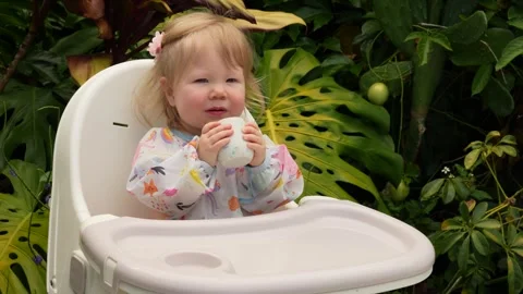 Cute toddler learning to sit on a plastic chair in a lush tropical garden, early Stock Footage 311654410