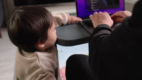 A cute toddler playing on the floor while his father works on a laptop Stock Footage 245424049