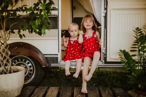 Cute toddler sibling girls wearing family look sitting on doorstep of the van Stock Photos