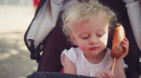 A cute toddler in a stroller eating a corn dog at a fair Stock Footage