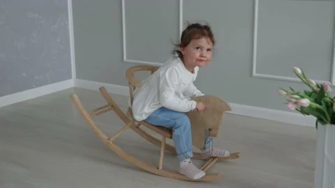 Cute two and half years old child girl swinging on a wooden horse indoors Stock Footage 237619591