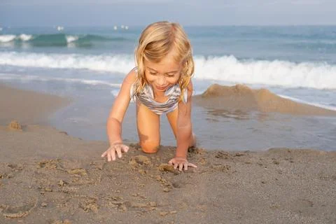 Cute two or three years old girl crawling on sandy beach , laughing, having fun Stock Photos