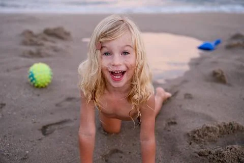 Cute two or three years old girl crawling on sandy beach , laughing, having fun Stock Photos