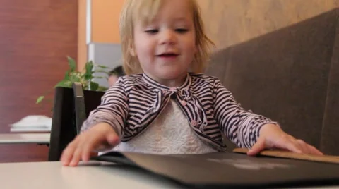 Cute two year old blond girl makes the order from the menu in a small restaurant Stock Footage 42197962