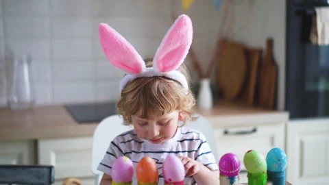 Cute two-year-old boy in bunny ears paint Easter eggs with multi-color paints si Stock Footage 170194358