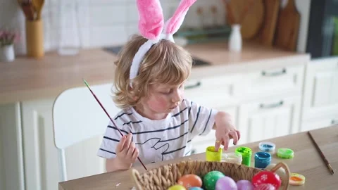 Cute two-year-old boy in bunny ears paint Easter eggs with multi-color paints si Stock Footage 170194621