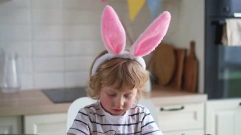 Cute two-year-old boy in bunny ears paint Easter eggs with multi-color paints si Stock Footage 170196248