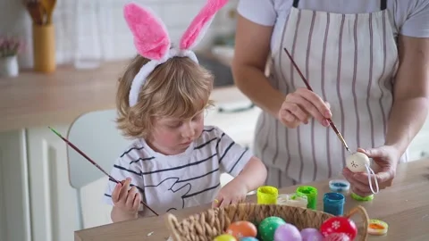 Cute two-year-old boy in bunny ears paint Easter eggs with multi-color paints si Stock Footage 170196511