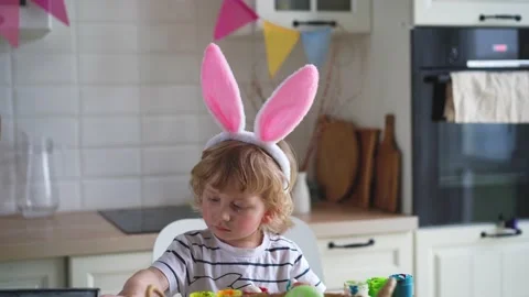 Cute two-year-old boy in bunny ears paint Easter eggs with multi-color paints si Stock Footage 170197384