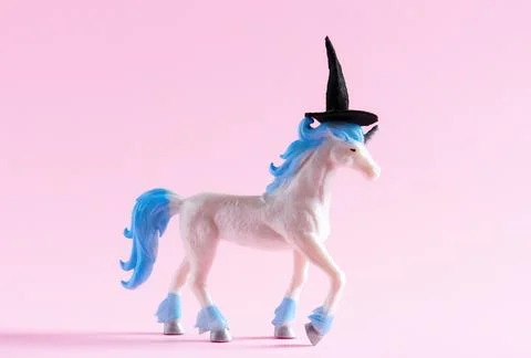 Cute unicorn toy wearing witch hat on pink background. Minimal art poster f.. Stock Photos