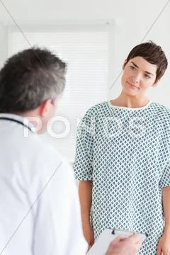Cute Woman in hospital gown talking to her doctor Stock Photos
