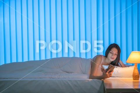 The cute woman lay on the bed and phone. Evening night time Stock Photos