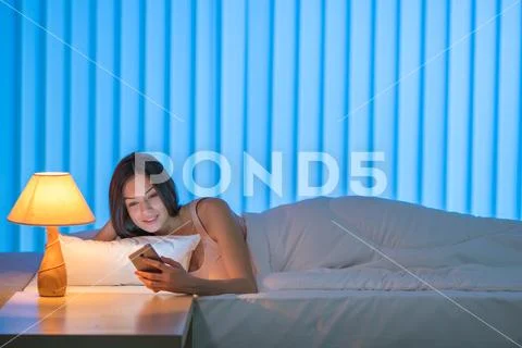 The cute woman lay on the bed and phone. Evening night time Stock Photos