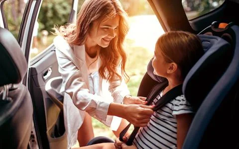 A cute woman mother put her daughter in a car seat and fastens her seat belts Stock Photos
