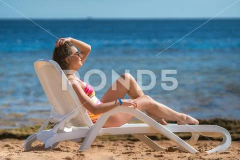 The cute woman sit on the sunbed on the sea background Stock Photos