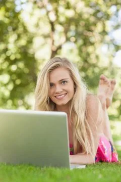 Cute woman using her notebook lying on a lawn Stock Photos