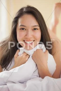 Cute young asian woman holding her duvet smiling at camera Stock Photos