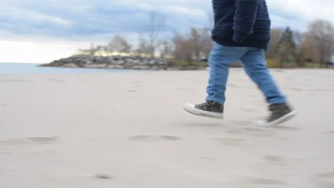 Cute young black boy running on beach towards water, wearing warm sweater. Stock Footage 88930727
