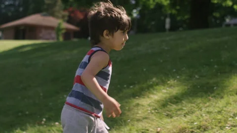 A cute young boy climbs a small grass hill while playing in the park Video stock 143635018