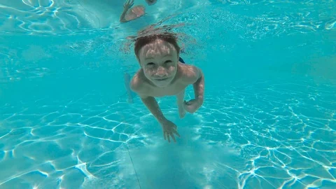 Cute young boy dives in blue pool with open eyes. Underwater viewpoint of pool Video stock 115330968